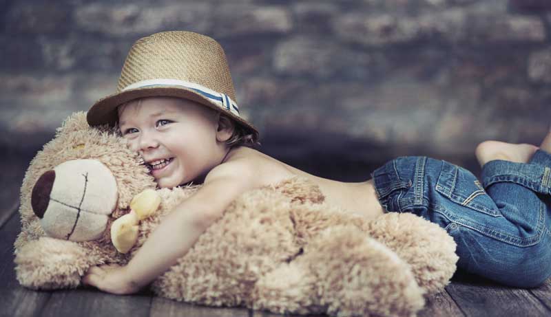 دانلود تصویر با کیفیت کودک در حال بغل کردن خرس قهوه ای